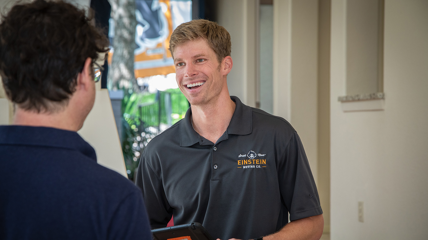 Cameron Brown, owner of Einstein Moving Company, smiles while talking to a man who has his back to the camera.