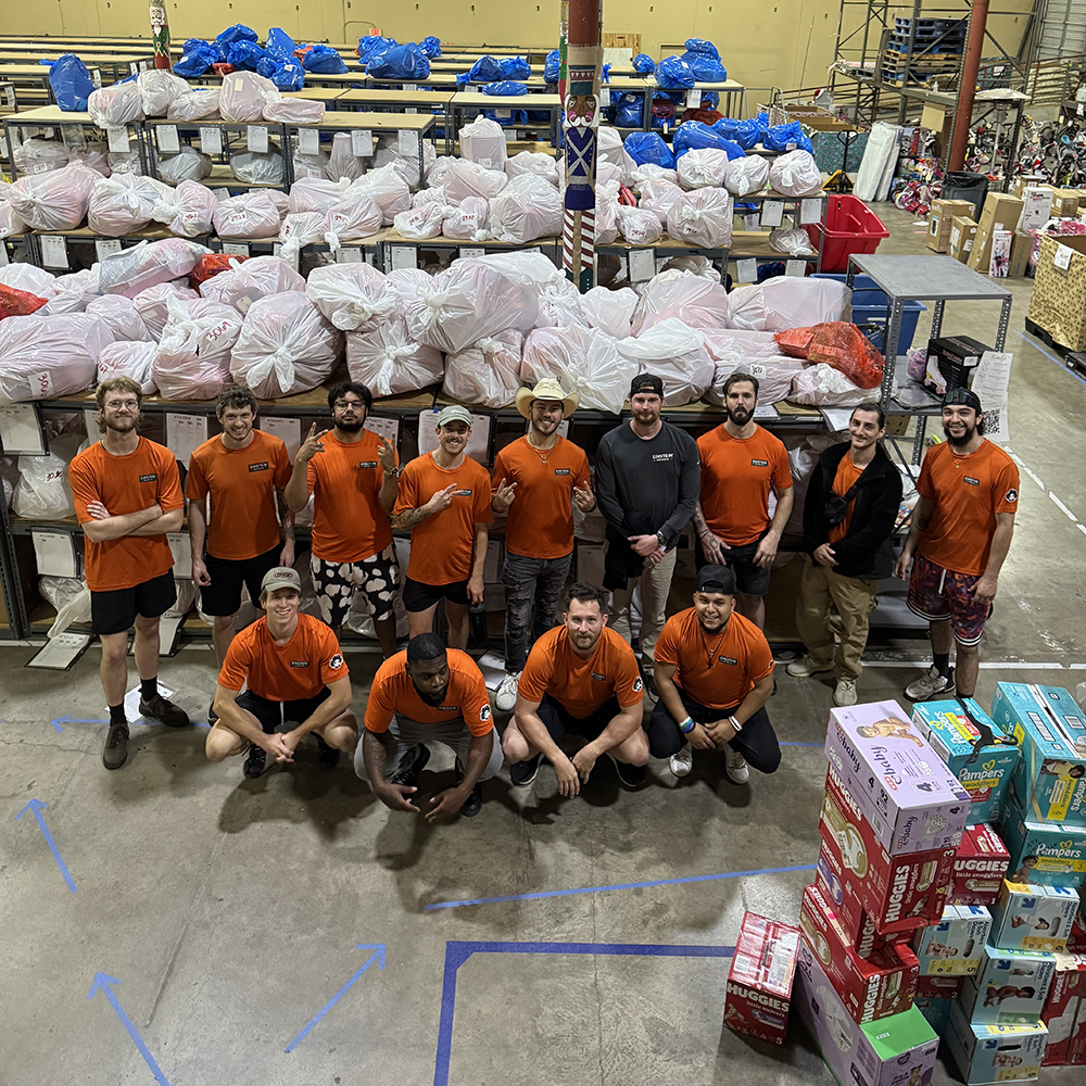 A team of movers standing as a group in a warehouse in front a large pile of bagged donations.