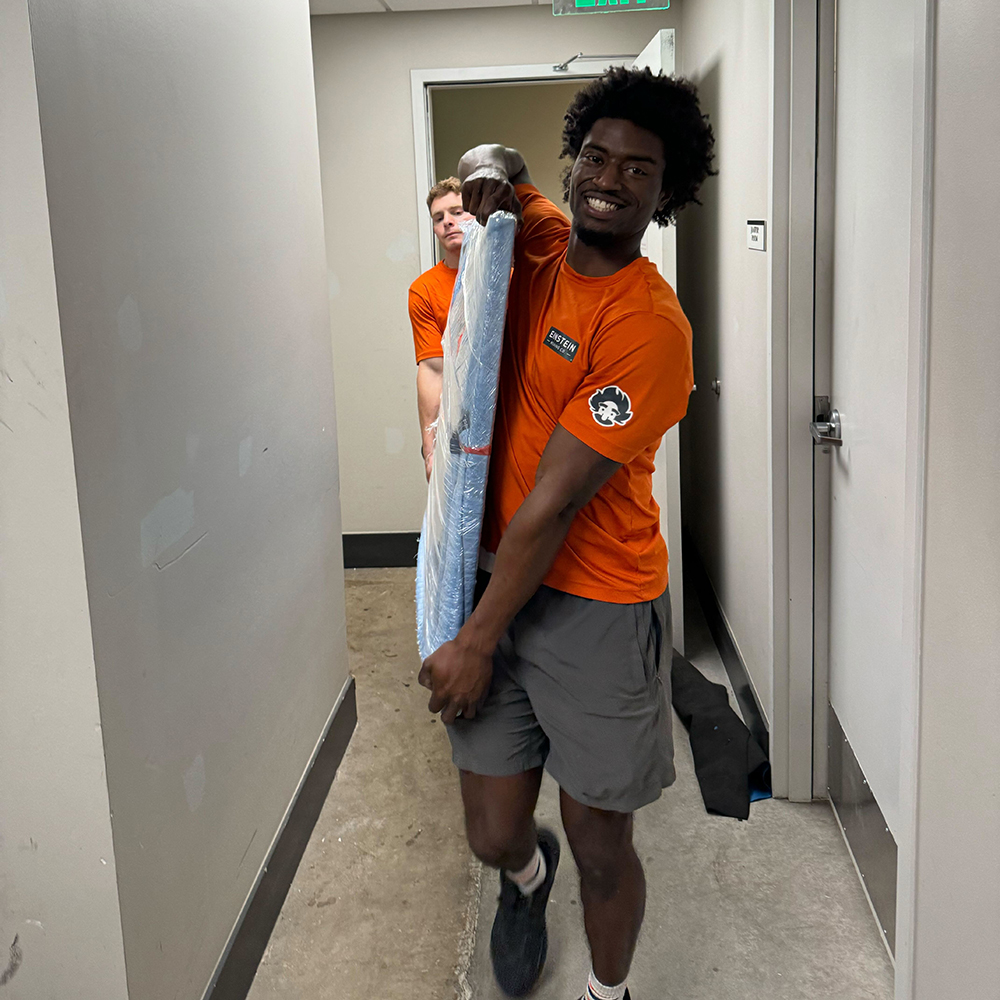 Two movers carrying a wrapped item carefully out of a hallway.