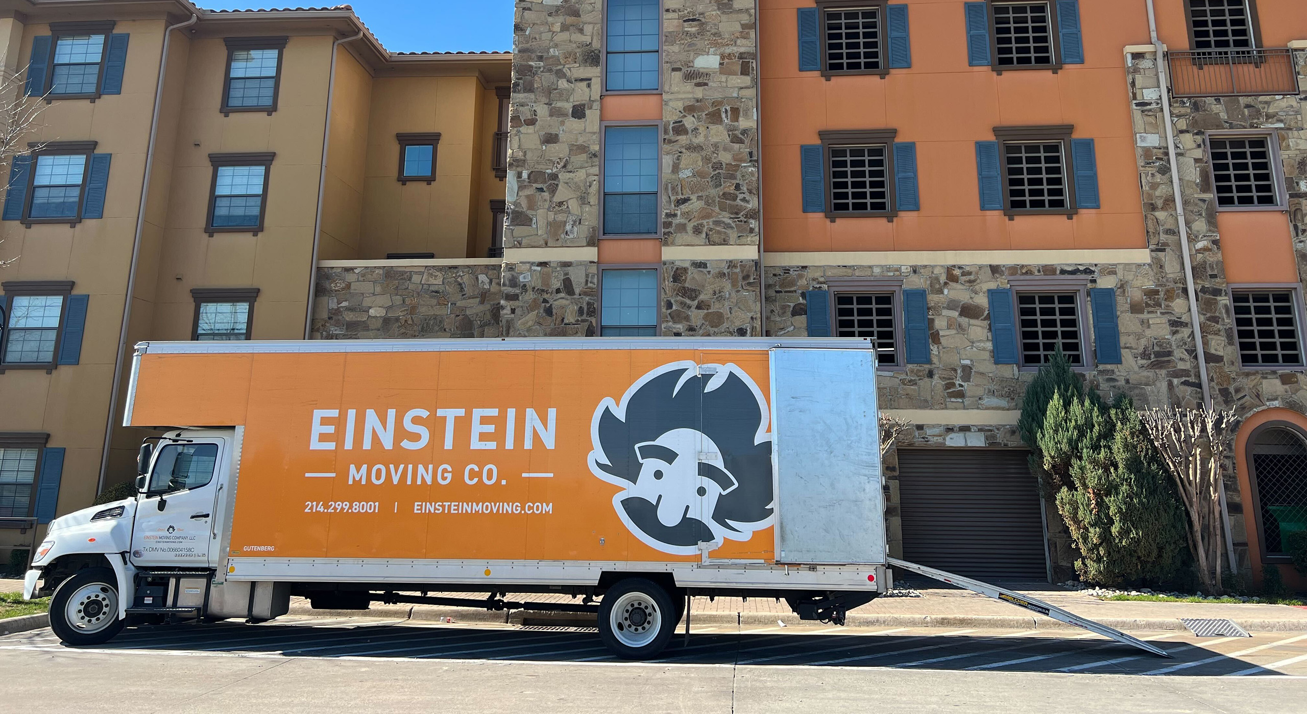 Einstein moving truck parked out front an apartment complex, with it's back doors open and a ramp coming out the back.