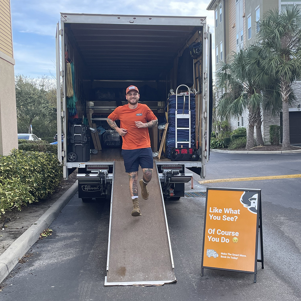 An employee of Einstein Moving Company walking down the ramp of an open moving truck parked outside a residential building.